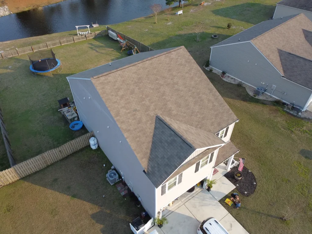 An aerial view of a house with a gray roof and white siding in a residential neighborhood